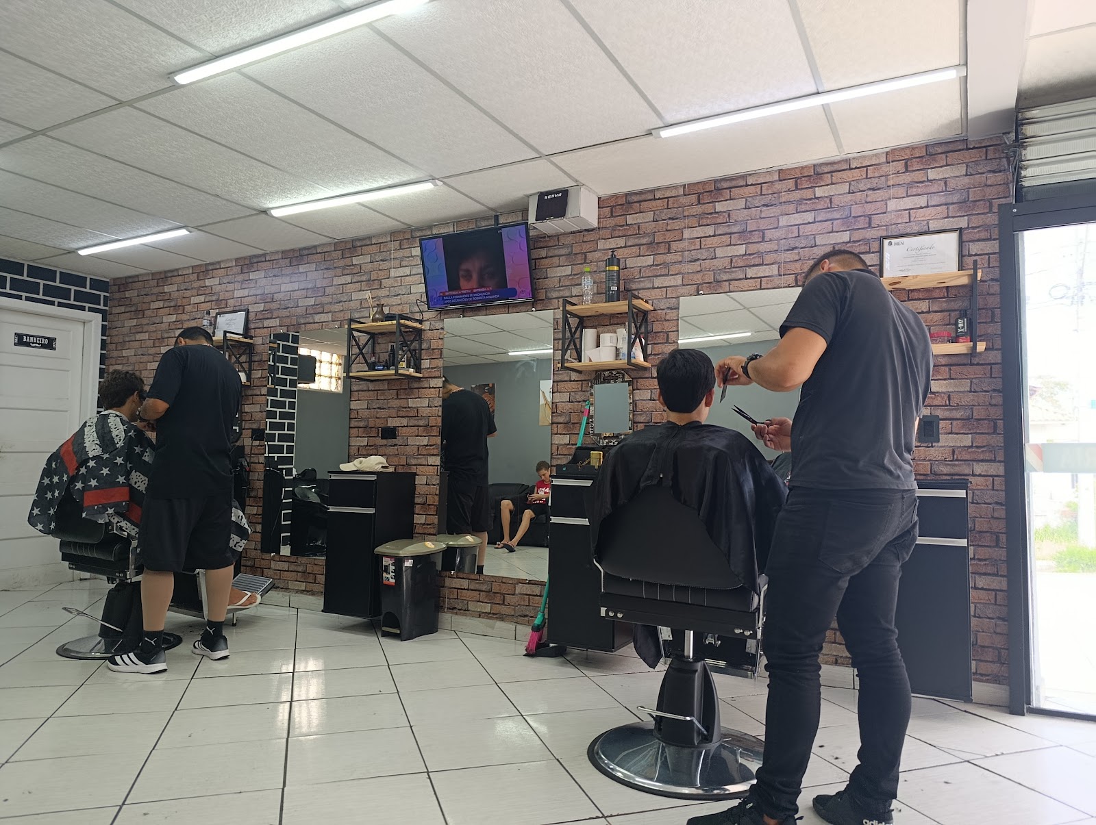 Barbeiros atendendo clientes na Barbearia Guih Santos, com parede de tijolo aparente
